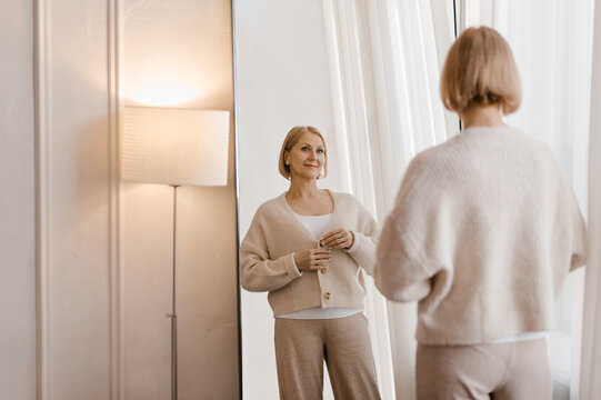 Mature woman buttoning jacket near mirror