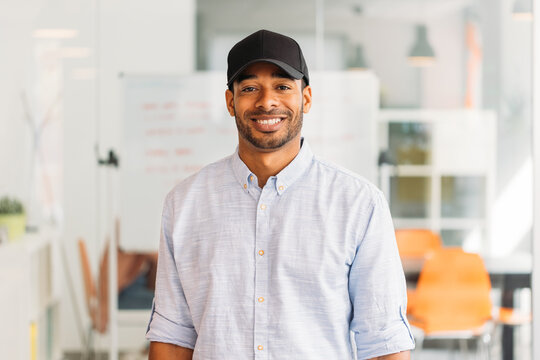 Cheerful creative black employee with black cap in modern office