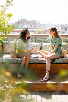 Happy diverse women resting on sofa and talking on terrace