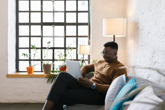 Young businessman sitting at the couch in the office using his laptop
