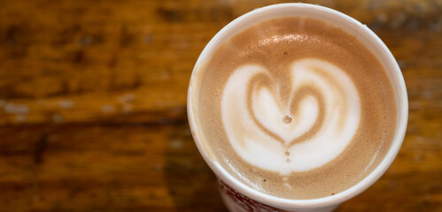 Table top view of a paper cup of hot latte coffee on wooden table. A latte is a coffee drink made with espresso and steamed milk.