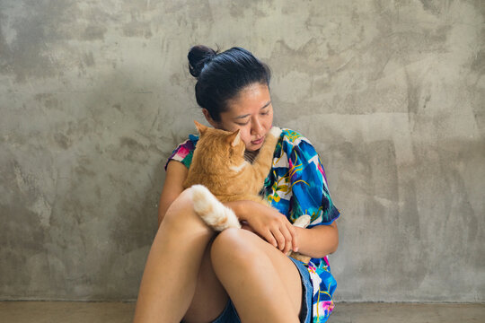 A sitting Asian woman hugging a cat