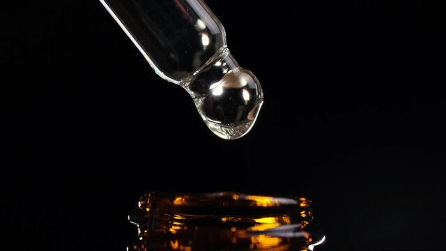 Closeup of cosmetics oils drips from pipette into bottle on black background.
