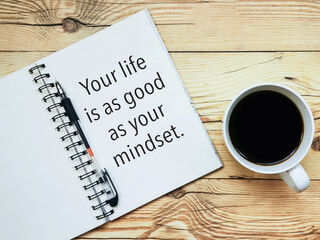 Open notebook with text "Your life is as good as your mindset" and a cup  of coffee on wooden background.