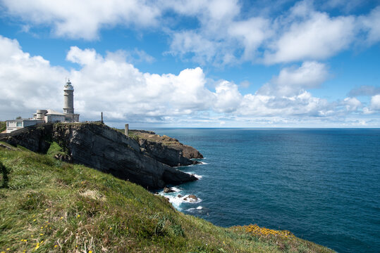 Old lighthouse on rocky cliff washing by blue sea in sunlight