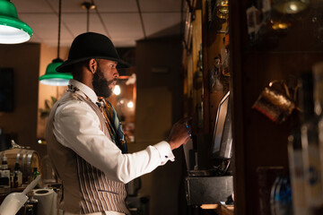 Black barman using cash register in bar