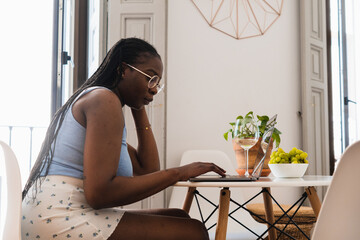 Young black lady with laptop and wine at home table