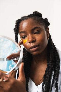 Black woman applying eye patches and looking in mirror