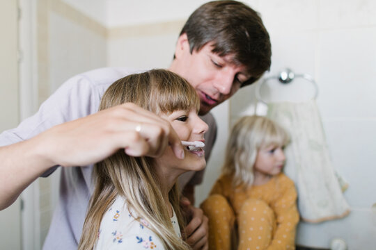 Father helps his daughter brush her teeth
