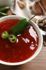 Spicy chili sauce in bowl on wooden table, closeup
