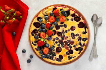 Strawberry blueberry pie decorated with fresh berries with a red napkin and spoons on a gray background, top view