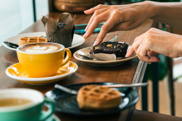 Young woman' s hand over a plate of cake, smartphone on the table. In the foreground is a cup of coffee