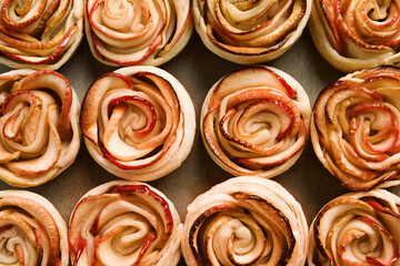 Obraz na płótnie Canvas Freshly baked apple roses on parchment paper, flat lay. Beautiful dessert