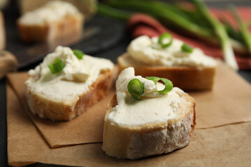 Bread with cream cheese and green onion on table, closeup