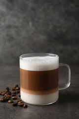 Hot coffee with milk in glass cup and beans on grey table