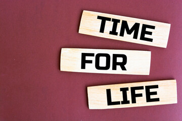 The words TIME FOR LIFE are written on scattered wooden blocks on a brown background. Business concept