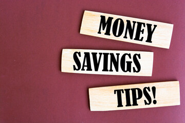 block with word 'money' on top of a blocks with words 'money savings tips'. Beautiful wooden table, brown background. Copy space. Business concept.