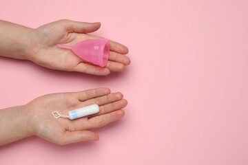 Woman holding menstrual cup and tampon on pink background, top view. Space for text