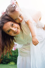Mom and daughter in white dresses have fun, play and cuddle on the lawn