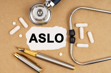 On the table is a stethoscope, pills, a pen and paper with the inscription - ASLO