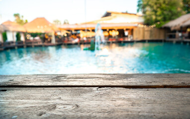 Image of wooden table in front of blurred background of pool and resturant.