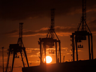 Fototapeta premium Industrial silhouette of wharf container cranes back lit by rising sun