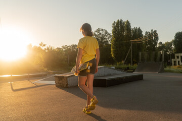 Naklejka na ściany i meble girl goes for a drive in the park on a skateboard. child goes in for sports at sunset.