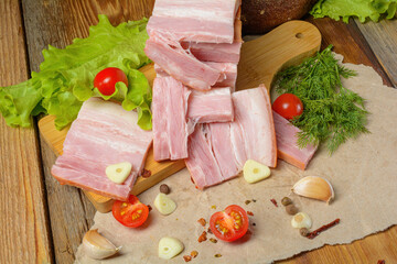 Smoked sliced pork belly, bacon, ham with herbs, tomatoes and black pepper on food paper. Wooden rustic background.Selective focus.