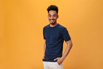 Man in black t-shirt smiles sweetly on orange background. Portrait of guy in blue tee posing on...