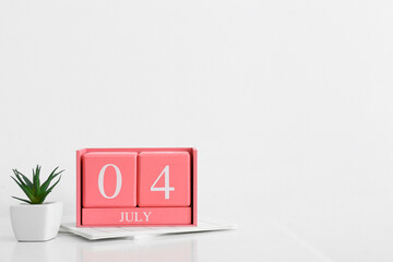 Cube calendar with date JULY 4, houseplant and notebooks on light background
