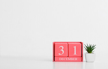 Cube calendar with date DECEMBER 31 and houseplant on light background