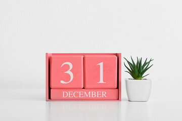 Cube calendar with date DECEMBER 31 and houseplant on light background