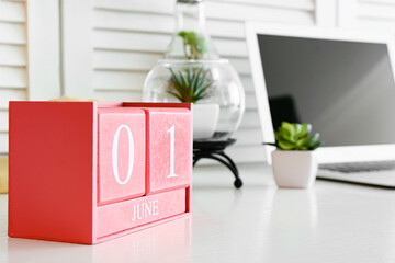 Cube calendar with date JUNE 1, houseplant and laptop on table in room, closeup