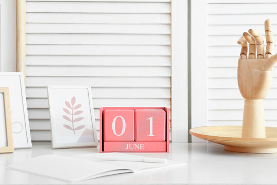 Cube calendar with date JUNE 1, frames and wooden hand on table in room