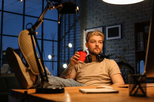 Young man drinking coffee while working late in evening