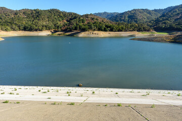 Looking down from the concrete wall of dam on almost dried with low water lever Stevens Creek reservoir in San Francisco Bay Area, California