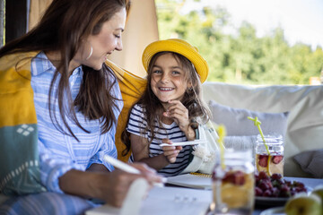 Focused mother and daughter looking paper schedule notebook together relaxing at outdoor terrace