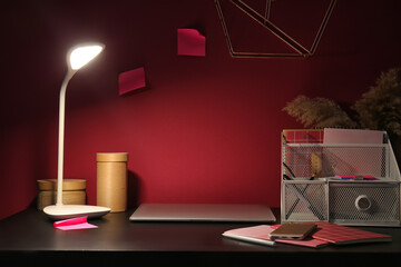 Modern workplace with glowing lamp in dark room