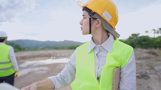Young female engineer wear safety gears looking at architectural blueprints drawing paper, structure planner real estate worker, safety first, outdoor construction site, manufacture project employee