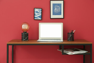 Modern workplace with laptop and lamp near color wall