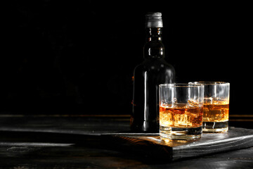 Bottle and glasses of cold whiskey on dark wooden background