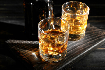 Bottle and glasses of cold whiskey on dark wooden background