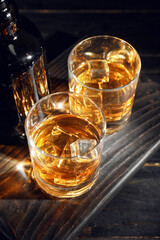Bottle and glasses of cold whiskey on dark wooden background