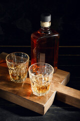 Bottle and glasses of cold whiskey on dark wooden background