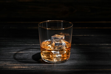 Glass of cold whiskey on dark wooden background