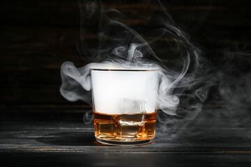 Glass of cold whiskey and smoke on dark wooden background