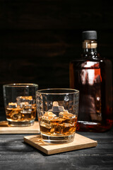 Bottle and glasses of cold whiskey on dark wooden background
