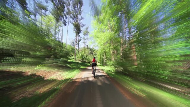 The rear view of the female cyclist riding a bicycle in the Divoka Sarka natural reserve in Prague on a sunny summer day.