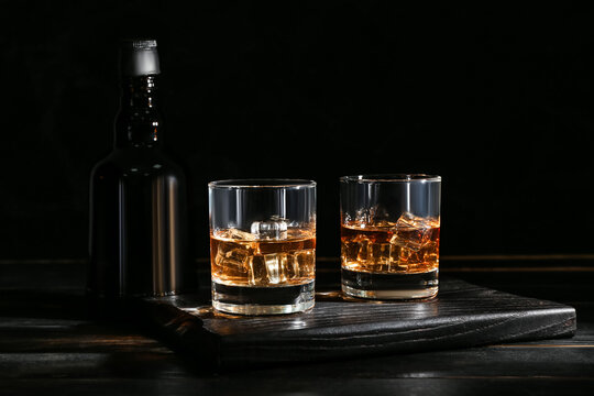 Bottle and glasses of cold whiskey on dark wooden background