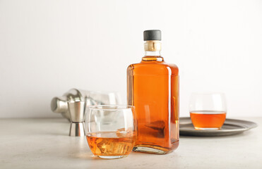 Bottle and glasses of cold whiskey on light background